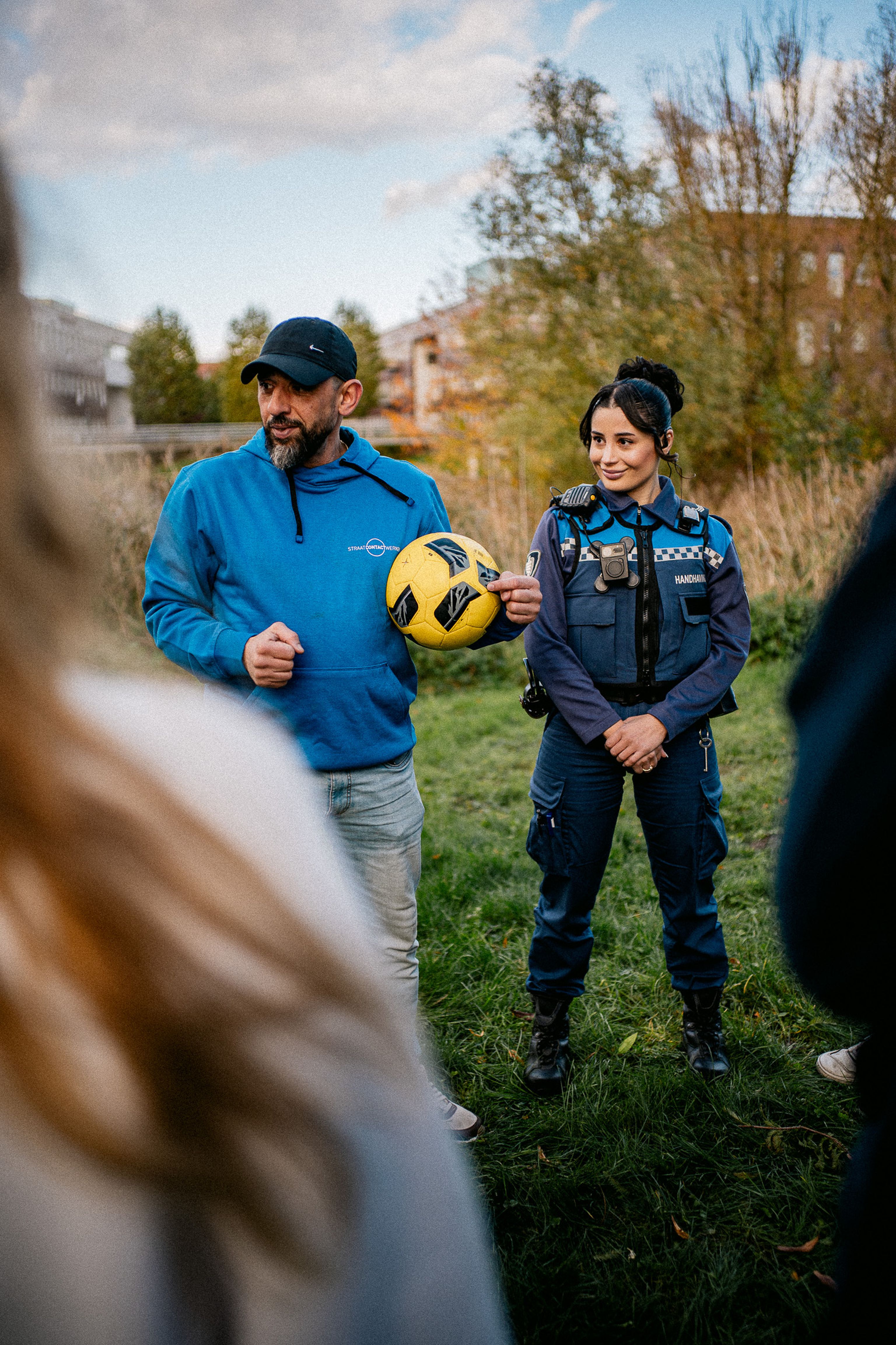 Jongerenwerker met bal in zijn hand en jeugdboa geven uitleg aan jeugdgroep over spel